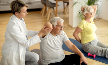 Female physiotherapist helping to senior couple with exercising at home.